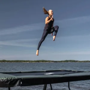 A woman bounce running on a trampoline with water in the background.