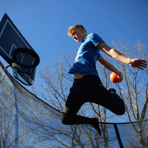 A boy on a trampoline, jumping like he is going to dunk on the Acon trampoline basketball hoop with net attached to the hoop.