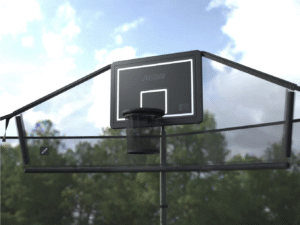 A black basketball with hoop and backboard with nets on the sides stands in front of trees under a partly cloudy sky.